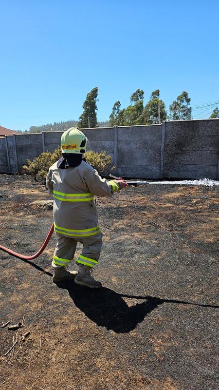 Voluntario con equipo de protección enfriando el terreno tras un incendio de pastizal